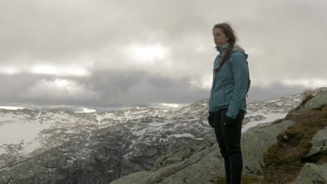 a woman takes in a snowy and rocky view from a high altitude mountain on a windy, overcast day in norway, slow motion