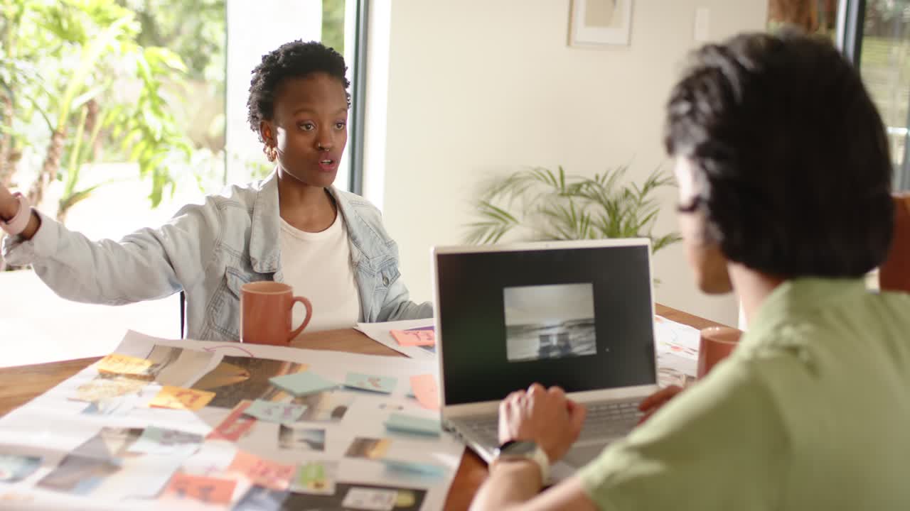 Diverse coworkers scrolling laptop then writing sticky notes refining ideas in sunlit workspace