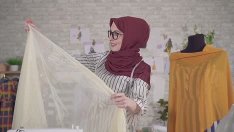 young muslim woman fashion designers in national headscarves in glasses working with fabric in studio