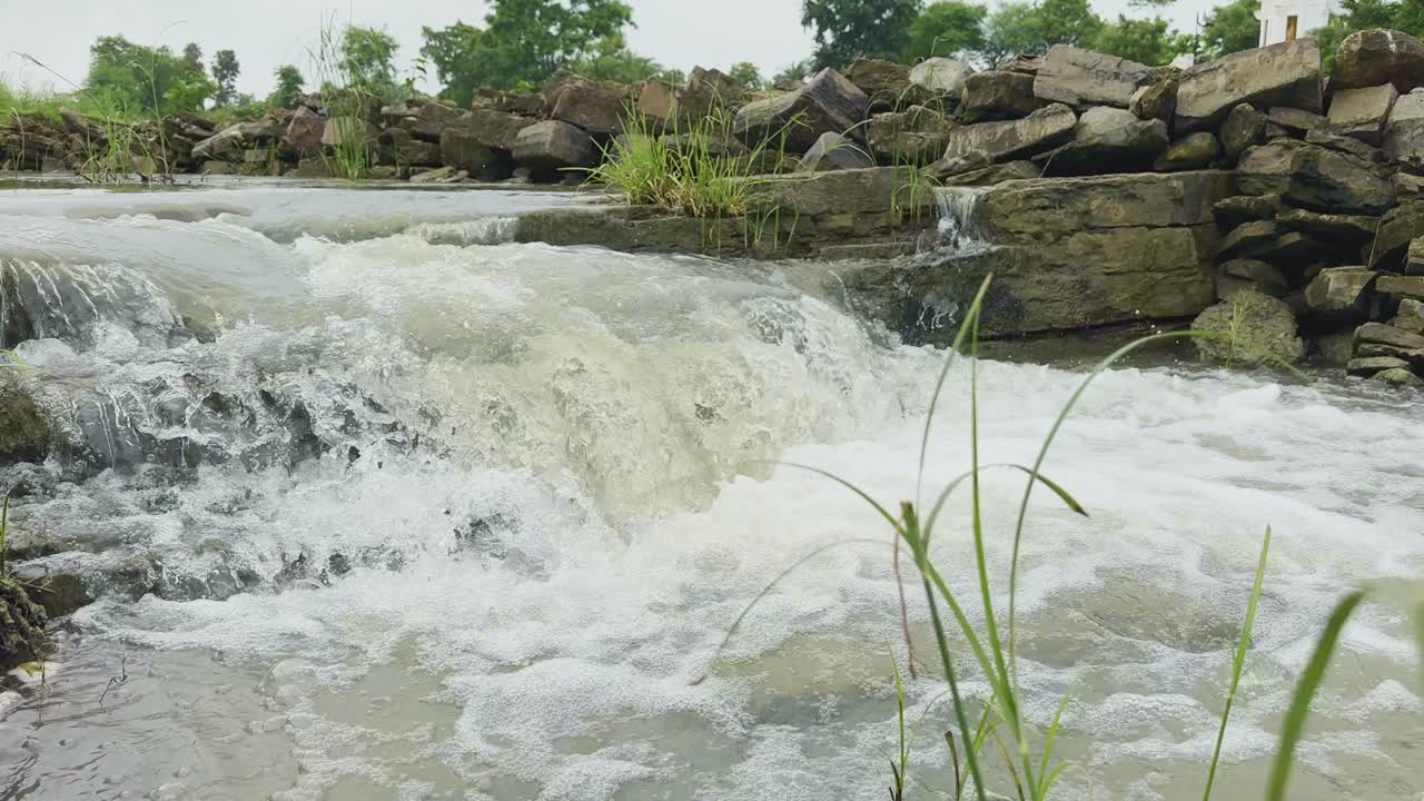 Closeup of a rocky cascade where water tumbles down over irregular rock formations amidst a lush, green environment, The dynamic flow of the water creates white foamy rapids, contrasting with the dark