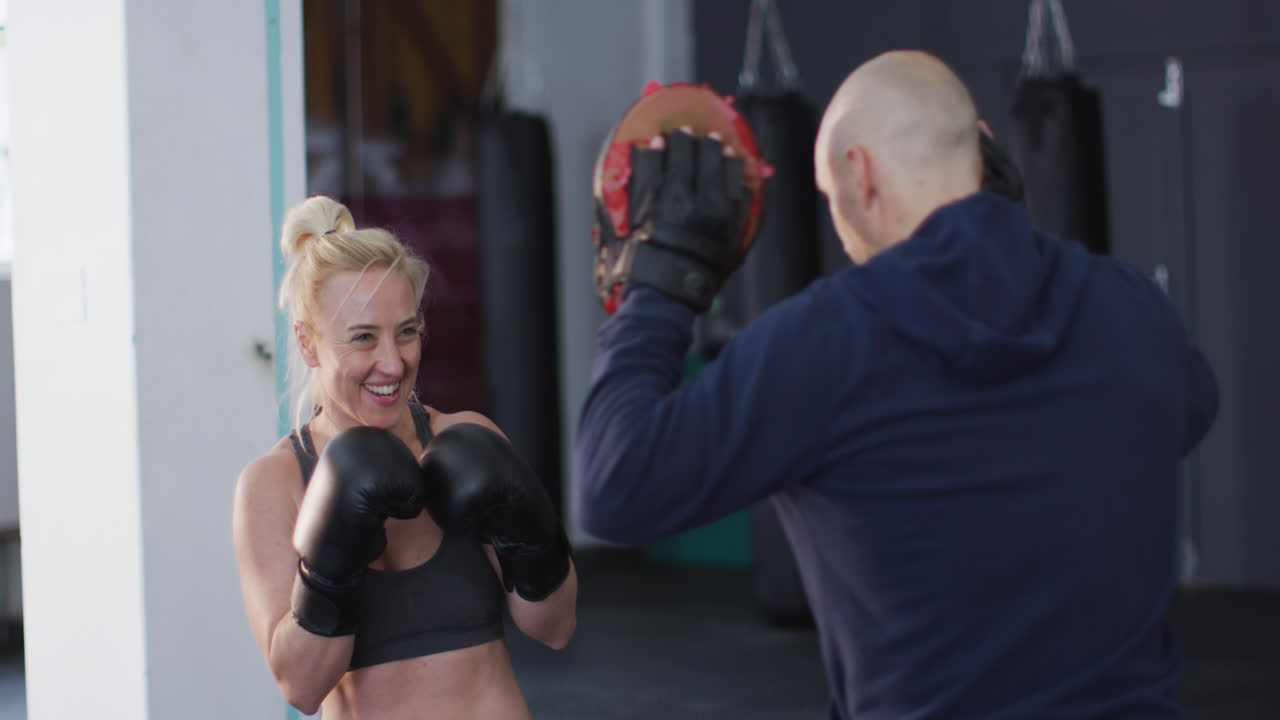 boxeadora caucásica con guantes de boxeo entrenando sus golpes con un entrenador masculino en el gimnasio