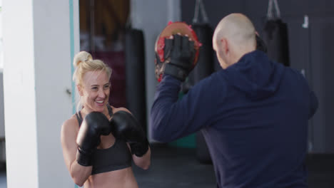 boxeadora caucásica con guantes de boxeo entrenando sus golpes con un entrenador masculino en el gimnasio