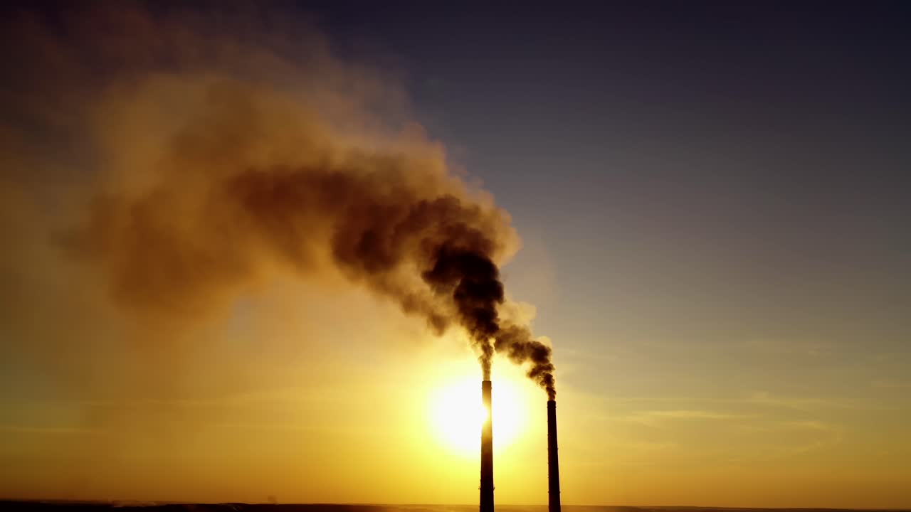 View of pipes with smoke. Power plant silhouette at sunset