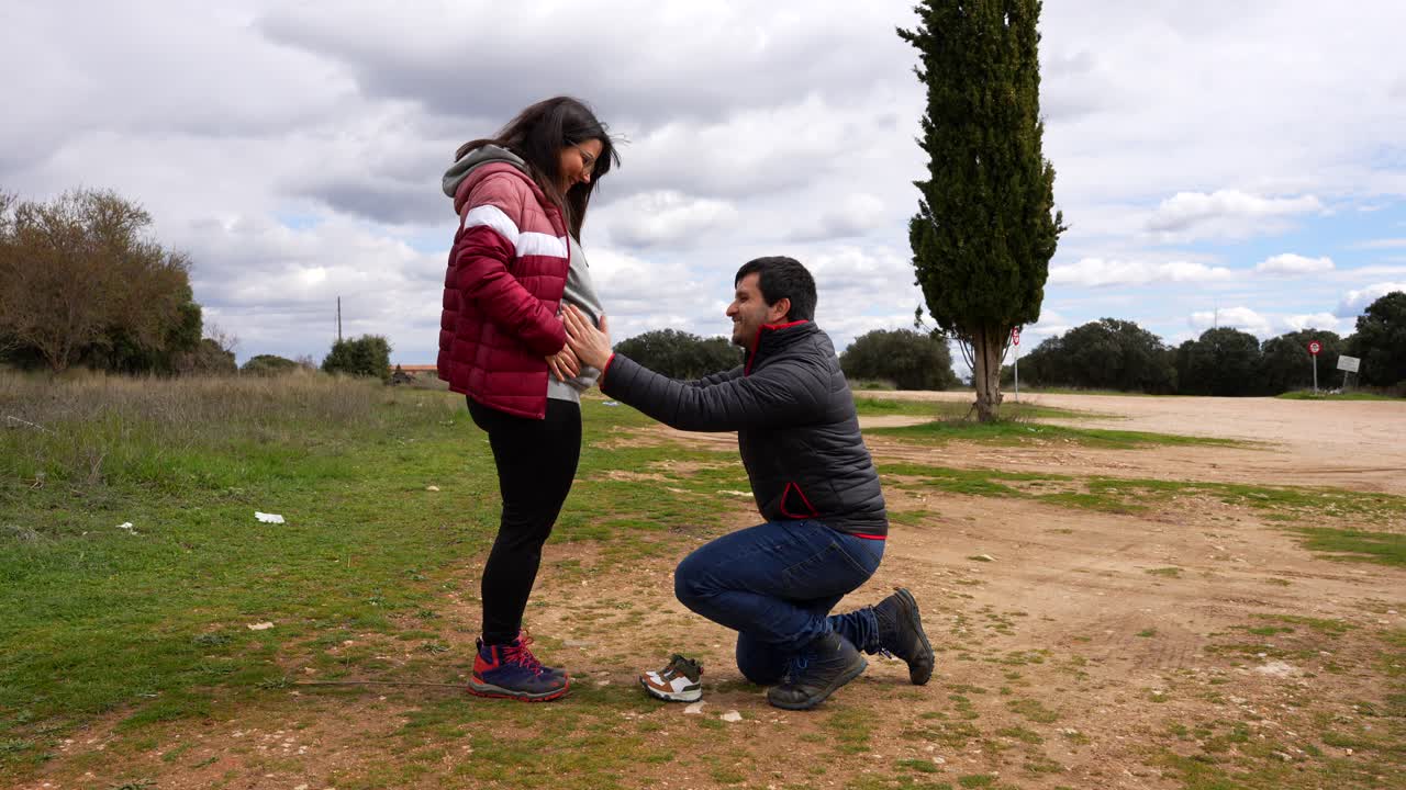 Pregnant couple walking in the countryside showing a pair of baby boots
