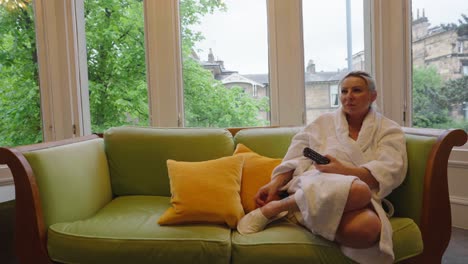 Woman-wearing-dressing-gown-on-sofa-and-holding-a-remote-control,-locked-off