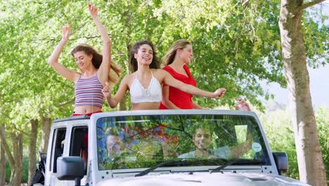 amigas de pie en la parte de atrás de un coche abierto bailando