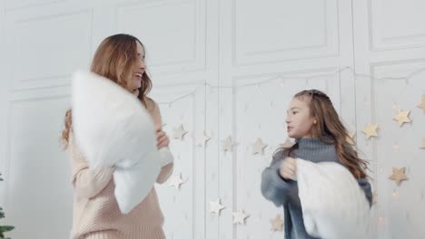 Closeup-mother-and-daughter-playing-with-pillows-on-in-sleeping-room-together.