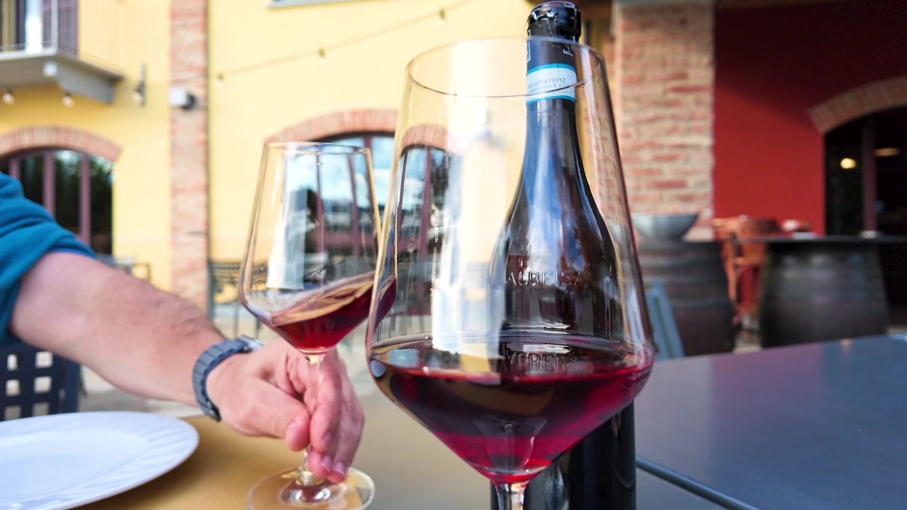 Un uomo allunga la mano per prendere un bicchiere di vino rosso italiano in un caffè all'aperto tra i vigneti.