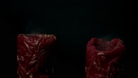 close-up shot of two red candles with intricate designs and rising smoke against a black backdrop, symbolizing the concept of death or endings. dramatic, moody lighting sets a somber tone