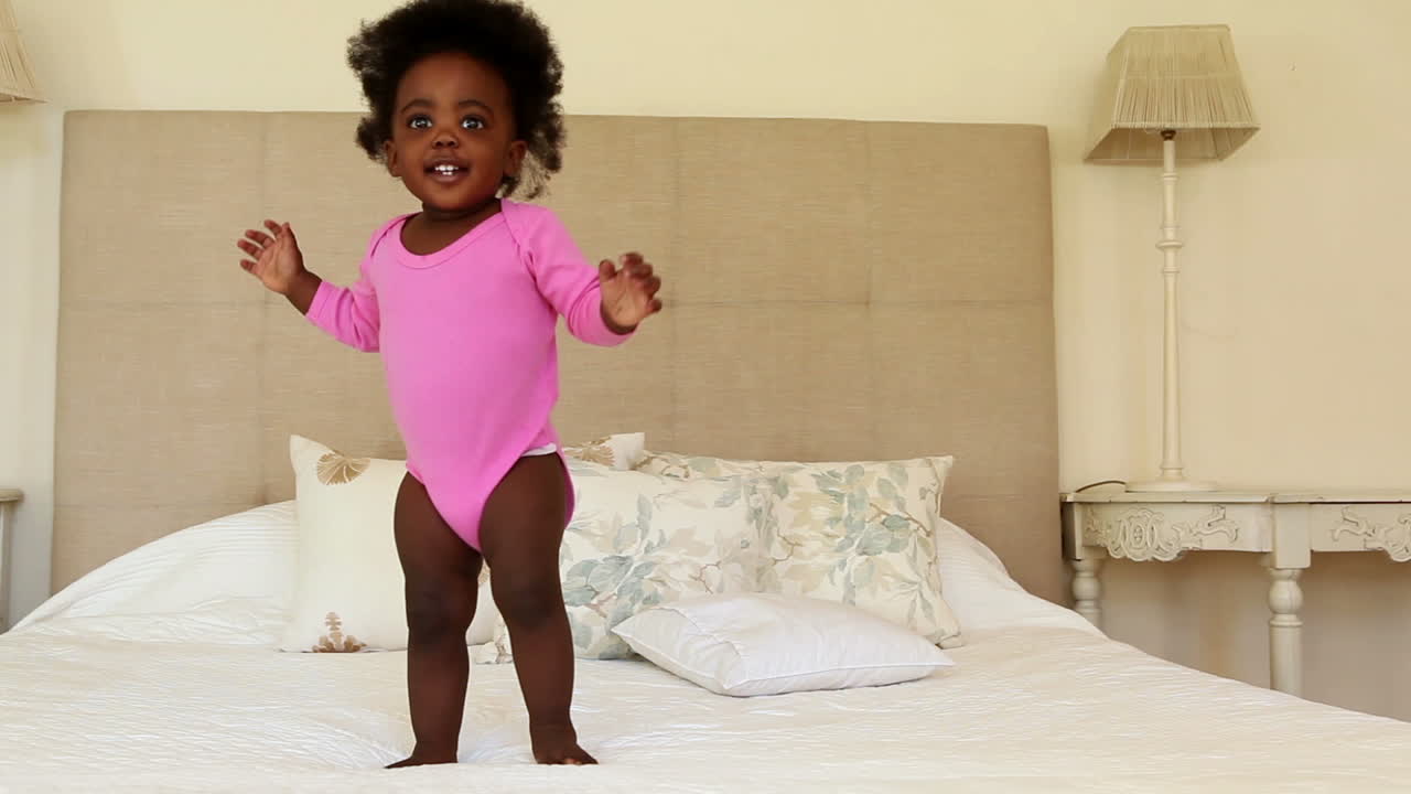 Cute baby girl standing and falling on bed