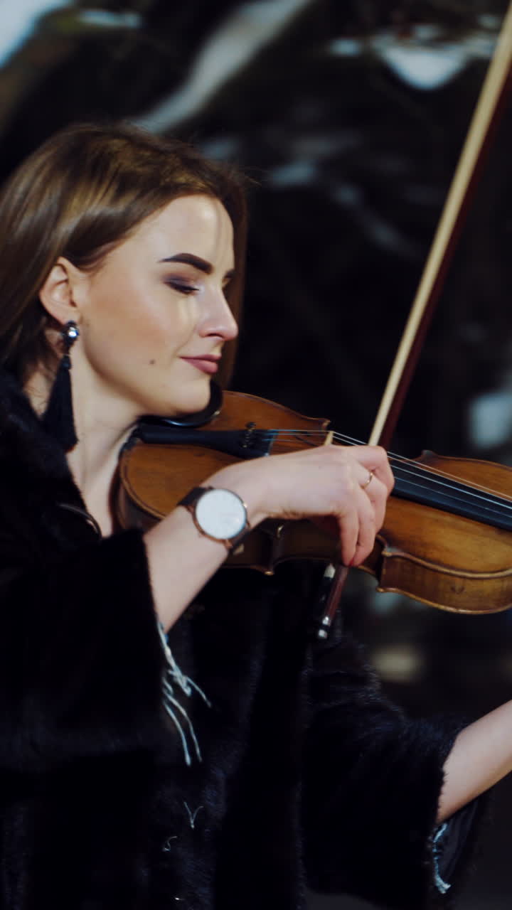 Musician playing on violin at night. Portrait of beautiful violinist playing at night winter street. Vertical video