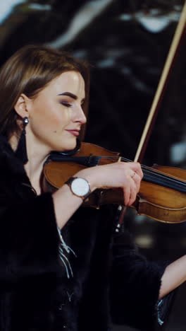 musician playing on violin at night. portrait of beautiful violinist playing at night winter street. vertical video