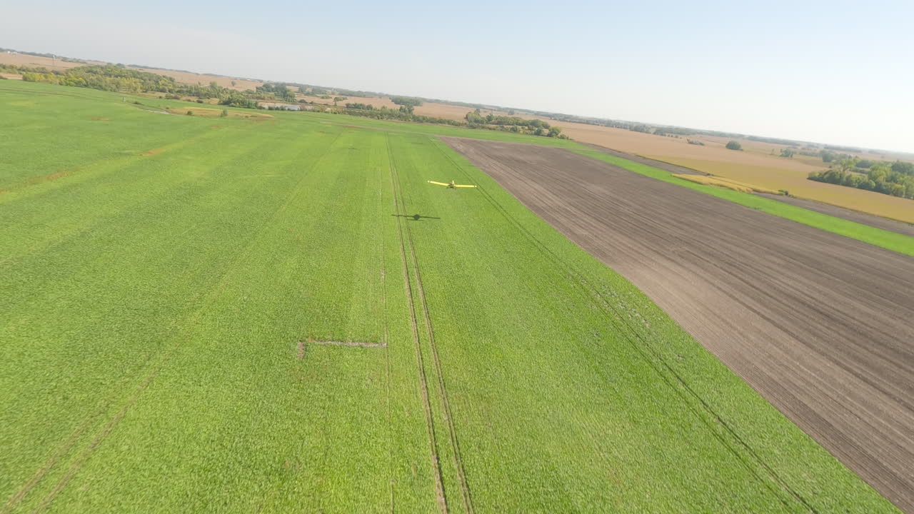 FPV Drone Captures Small Crop Duster Skimming Low Over Rural Airport's Grass Takeoff Area