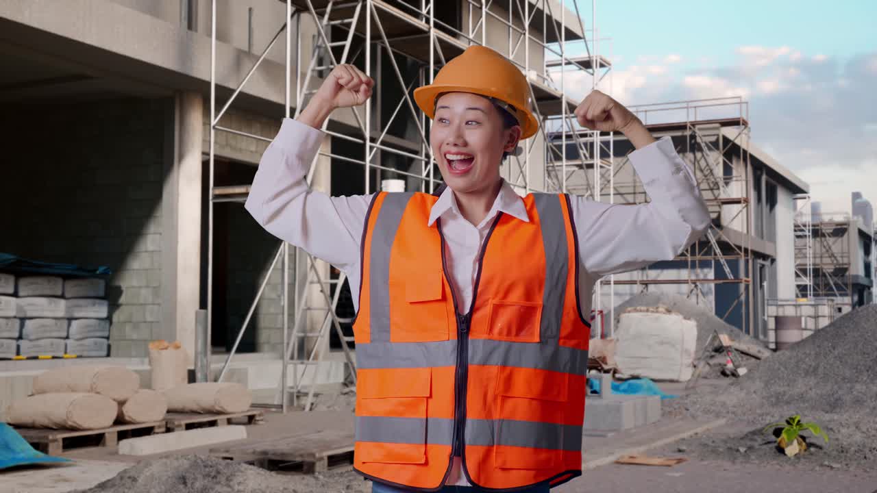 Asian Female Engineer With Safety Helmet Flexing Her Bicep And Smiling To Camera While Standing At Construction Site in Progress to New House