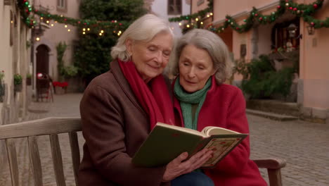 two elderly women reading a book on a decorated street during christmas