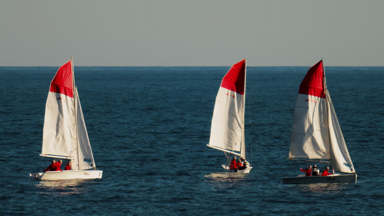 La Condamine, Monaco - February 8, 2025: Sailboats with red and white sails with people dressed in red uniforms