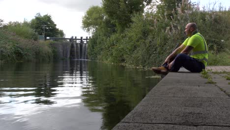 warehouse worker taking a break to relax, sitting at the concrete edge of the river canal in dublin, ireland