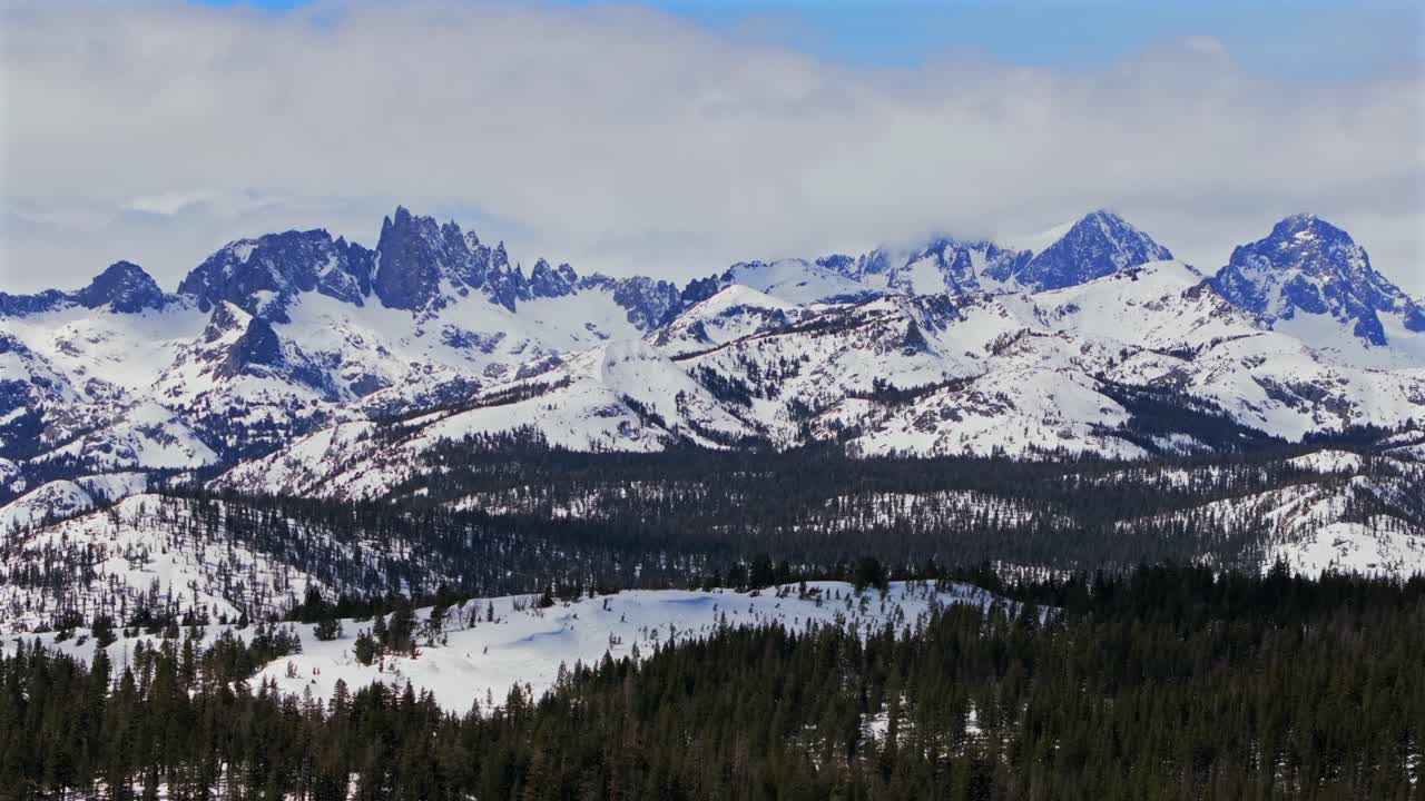 The stunning winter spring snowy jagged towering peaks of the Minarets Summit Mountains Mammoth Lakes California aerial drone sunny clouds daytime deep backcountry snow PCT vista point upwards jib
