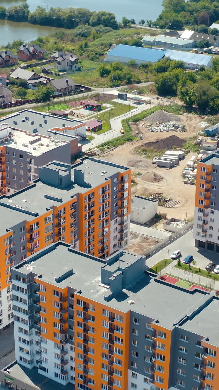 Modern urban housing on nature background. Construction site of a new residential area in the outskirts of a city. New multi-storey apartments. Aerial view. Vertical video