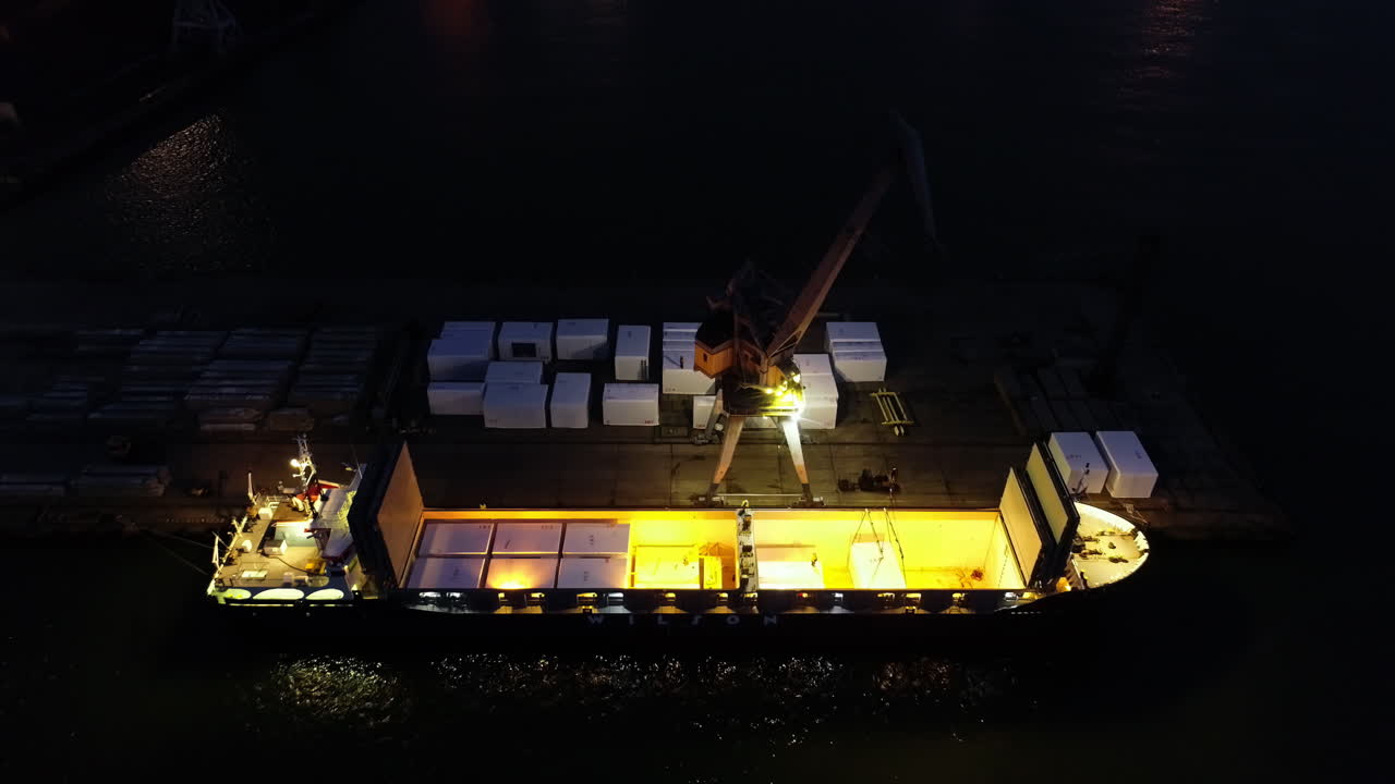 Nighttime aerial view of a cargo boat on the harbor dock with crane for lifting goods