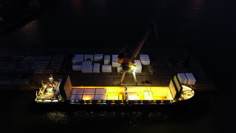 Nighttime-aerial-view-of-a-cargo-boat-on-the-harbor-dock-with-crane-for-lifting-goods