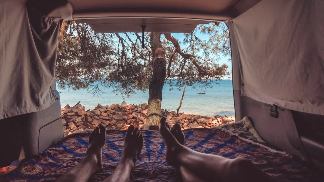 Young couple in van by the sea, feet view through back doors, cinemagraph with gently moving waves