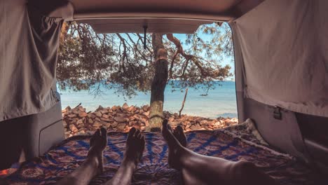 young couple in van by the sea, feet view through back doors, cinemagraph with gently moving waves