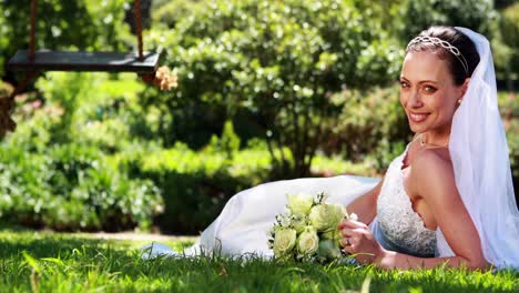 Pretty-bride-smiling-at-camera-lying-on-the-grass