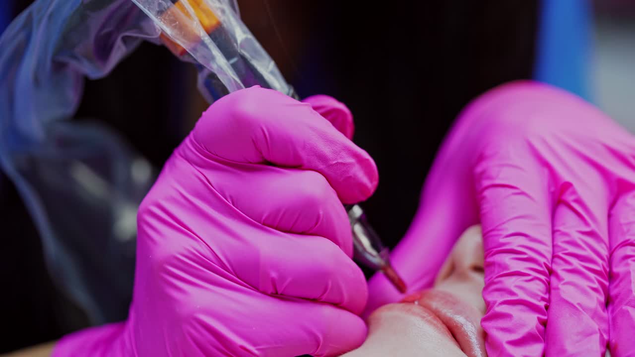 Lips micropigmentation. Cosmetologist applying permanent makeup on lips with a tattoo machine. Cosmetology procedure. Close-up.