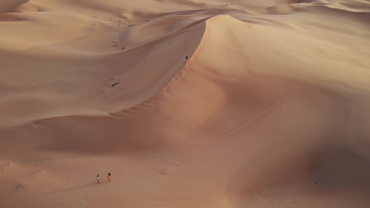 Vista aerea da drone che si allontana da un giovane uomo che cammina verso la cima di una duna nel deserto di Abu Dhabi, Emirati Arabi Uniti.