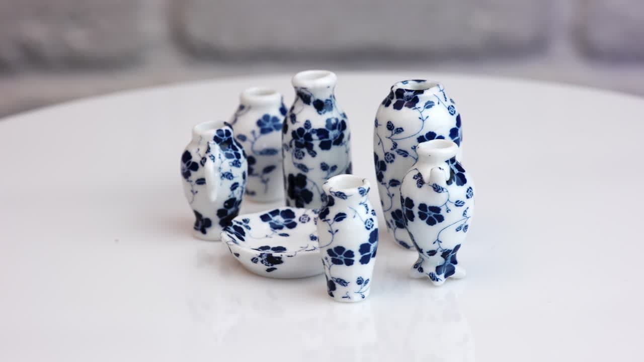 Diverse vases with blue flower print and a plate at the rotating table. Adorable miniature crockery close up.