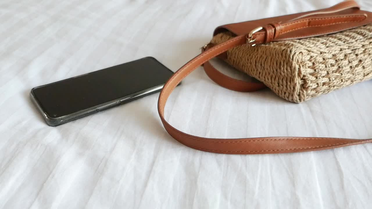 Smartphone e borsa di paglia su un letto