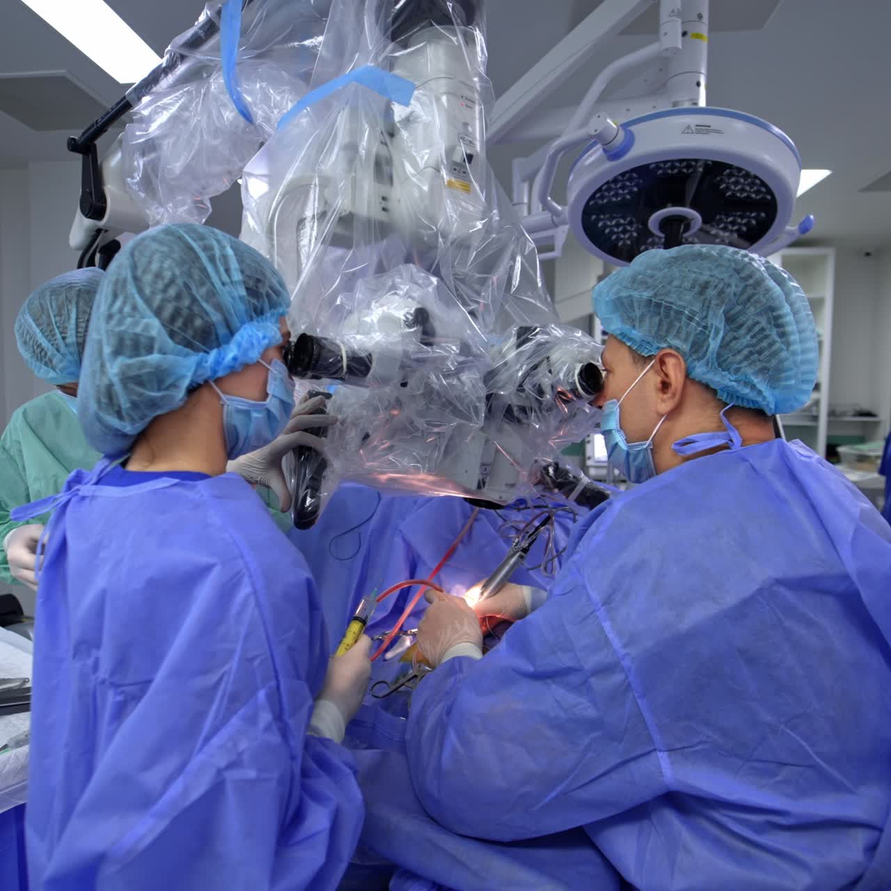 Neurosurgeon using powerful modern high-precise microscope at operation. Female assistant holding a syringe and male assistant preparing tools