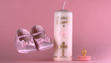 Baby-shoes-falling-beside-baptism-candle-and-pacifier