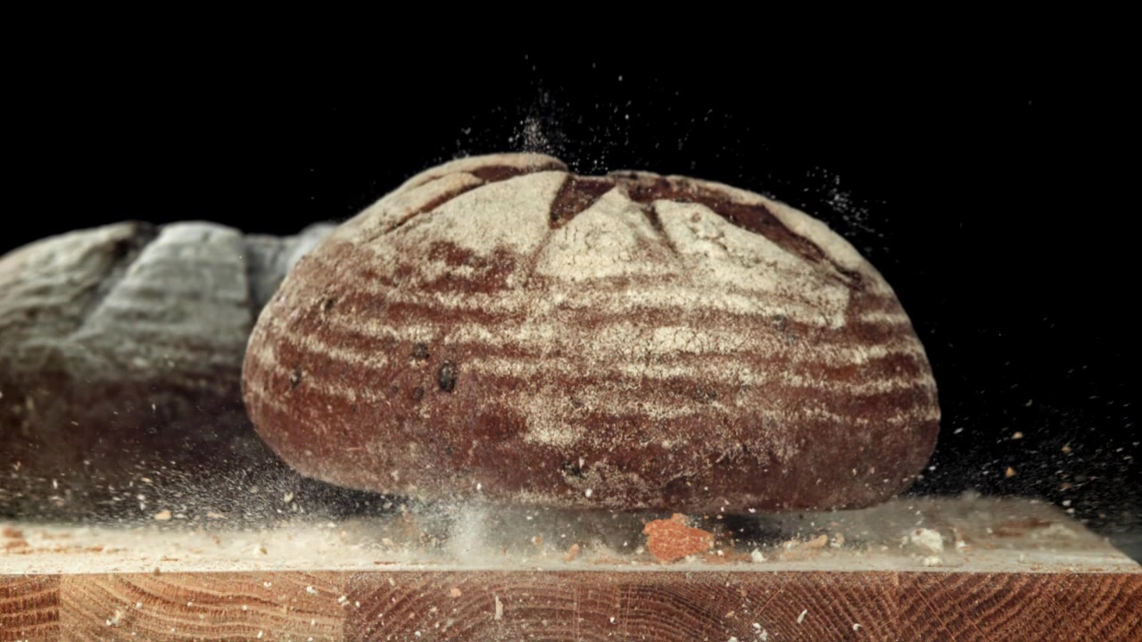 Freshly Baked Rye Bread Loaf Falling onto a Wooden Board