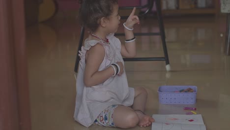 A-little-girl-sitting-on-a-floor-telling-her-mother-a-story-and-explaining-how-she-plans-to-colour-in-the-drawing-in-her-colouring-book