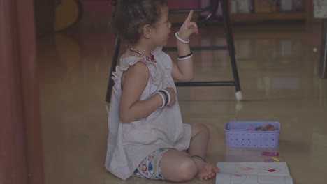 una niña sentada en el suelo contándole una historia a su madre y explicando cómo planea colorear el dibujo en su libro para colorear