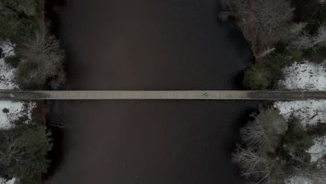 hombre caminando a través de un estrecho puente sobre el río tranquilo en vallee bras-du-nord en quebec, canadá - toma aérea de drones