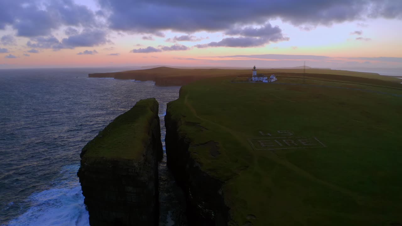 Aerial view of Loop Head Peninsula at sunrise, highlighting the sea stack, lighthouse, and Éire sign.
