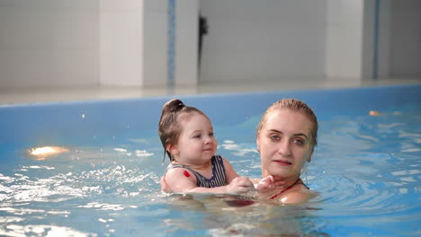 young mom in the pool playing with her baby daughter in slow motion. sports family engaged in an active lifestyle