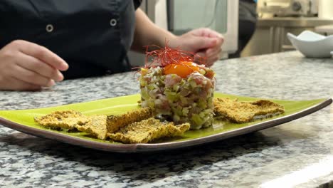 woman presents finished dish while another woman is cutting vegetables behind