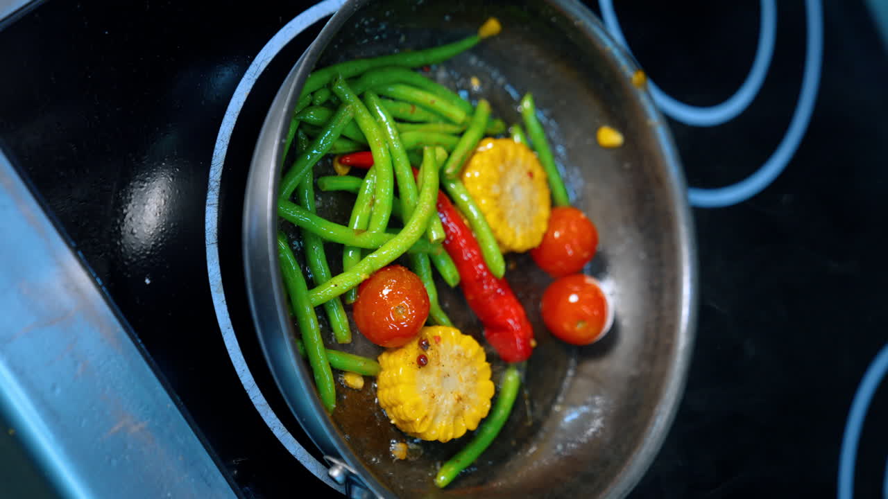 Tomatoes, maize and beans are cooked on the stove. Fresh vegetables are fried in the frying pan. Close up. Vertical view.