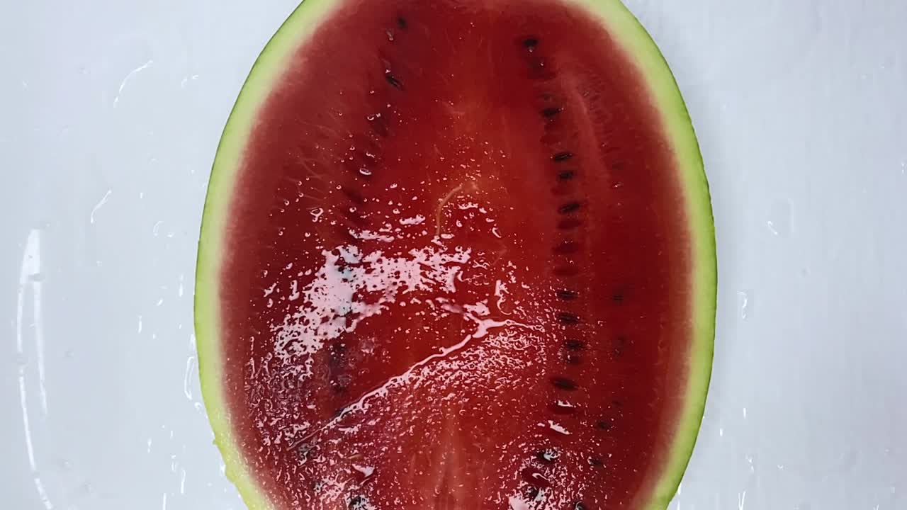 el chorro de agua cae sobre la sandía madura roja jugosa cortada por la mitad y cae en el spray