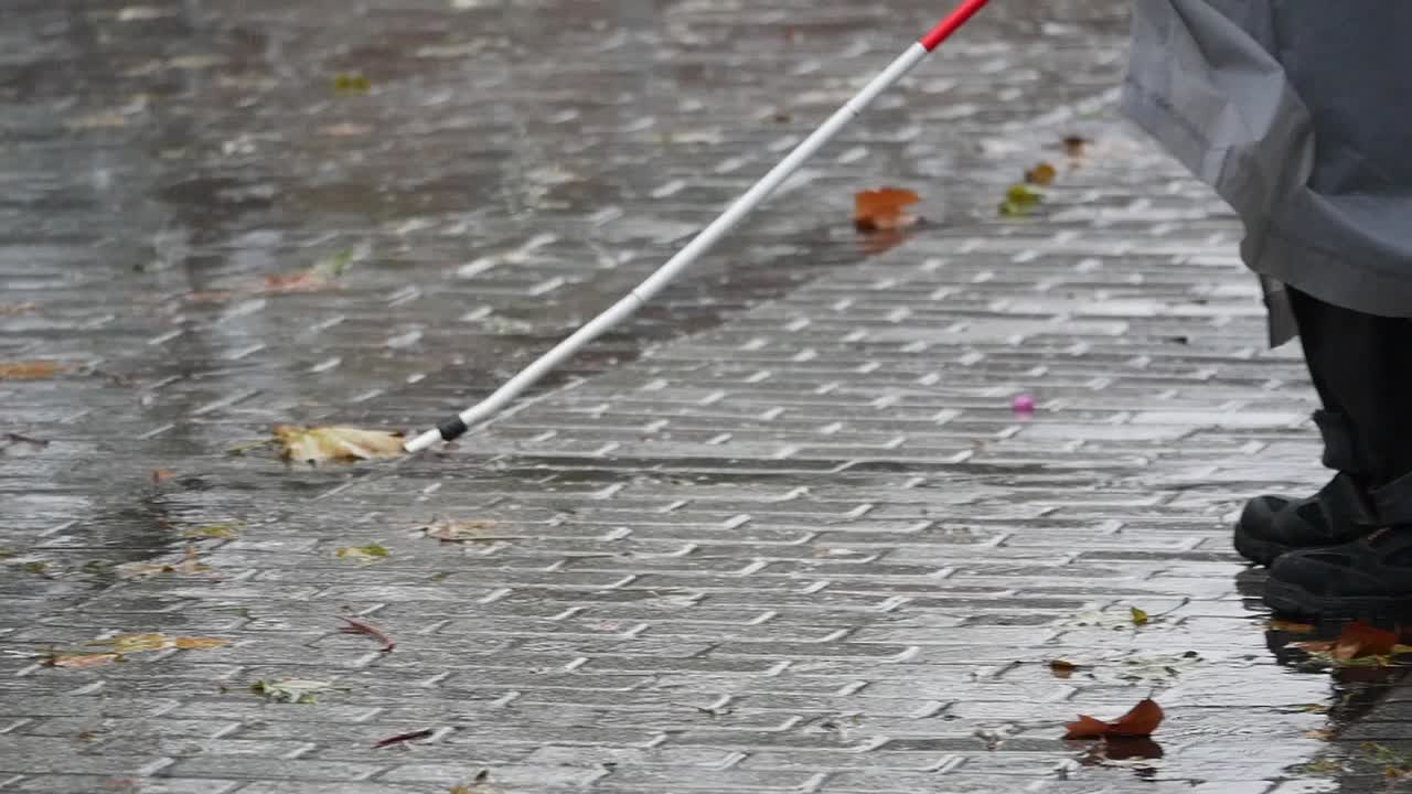 Person with white cane walking on a wet street in the rain