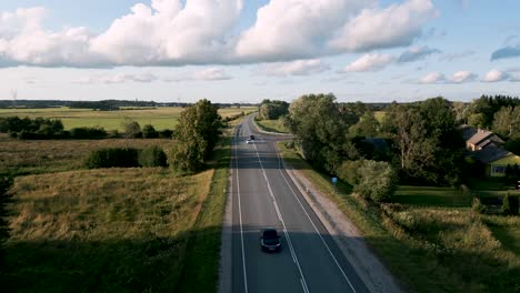 estonia - aerial drone flightover country road with overtaking cars - flyover following a romantic street with upcoming cars in a travel atmosphere with cloudy blue sky