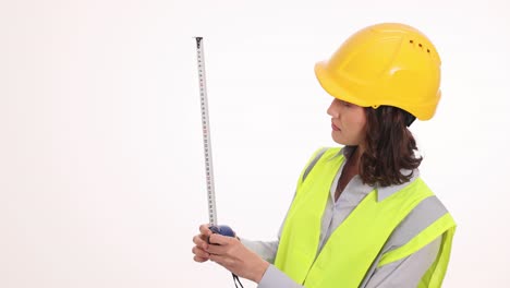 woman in hard hat and safety vest measuring with tape