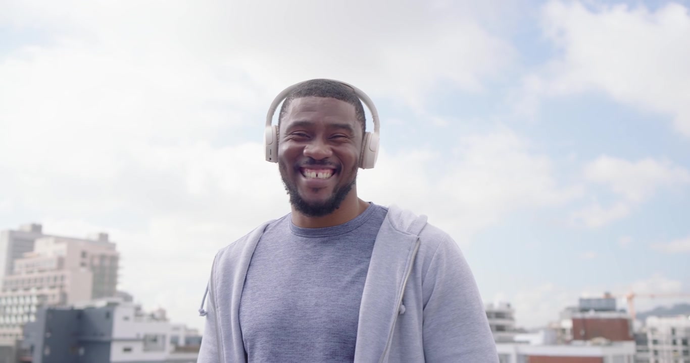 Uomo africano su un tetto che guarda il telefono, toccando lo schermo, controllando la musica con le cuffie, annuendo e sorridendo.