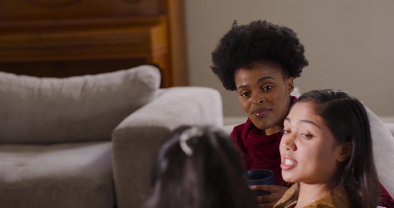 Donne di diverse etnie che rispondono a una domanda adolescenziale sul divano, con una donna indiana che parla e una donna afroamericana con una tazza.