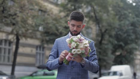 novio con una barba negra con un ramo de bodas en la calle. día de la boda