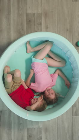 geschwister genießen es, in einem cyanfarbenen weichen pool in der nähe eines teppichs auf dem boden zu liegen.